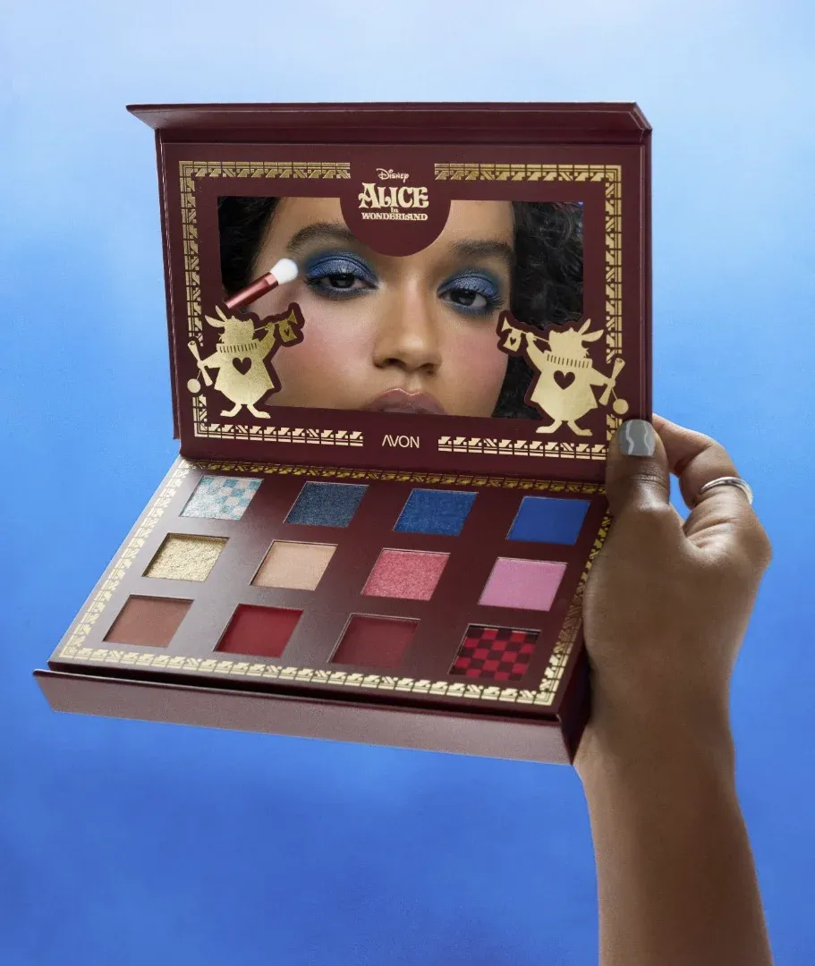 Modelo com maquiagem azul segurando aberta a paleta em formato de livro da Avon Alice no País das Maravilhas
