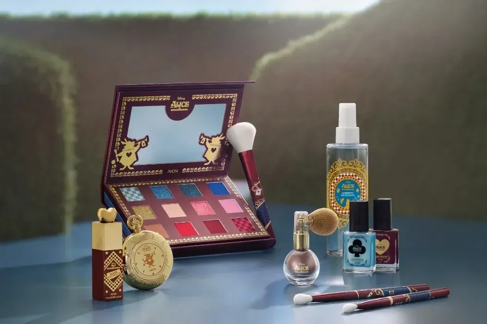 Paleta, gloss, esmaltes, body splash e iluminador da coleção Avon Alice no País das Maravilhas sobre uma mesa
