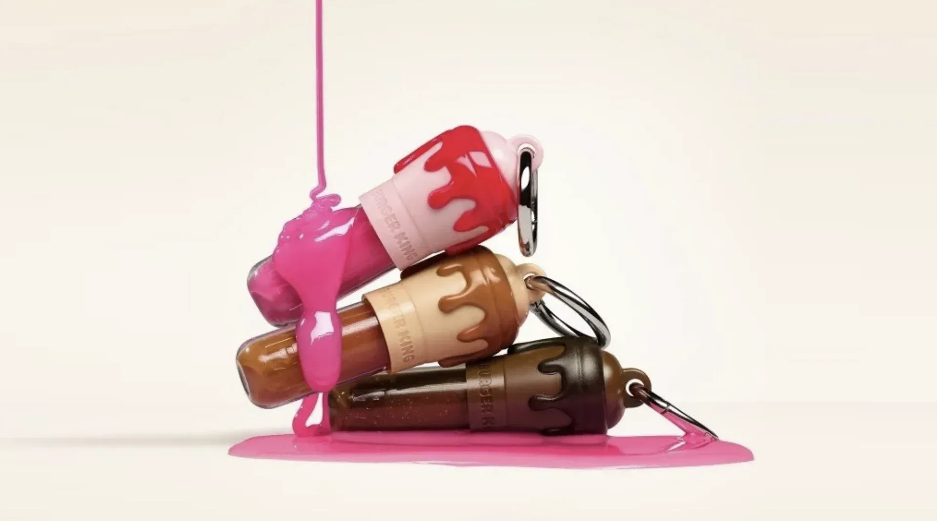 Três glosses LipShakes da FRAN com Burger King empilhados, nas cores morango, doce de leite e chocolate, com mosquetão prateado