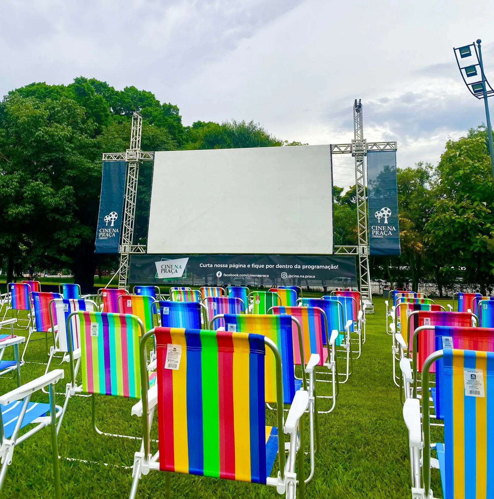 Cadeiras de praia coloridas enfileiradas diante do telão do Cine na Praça