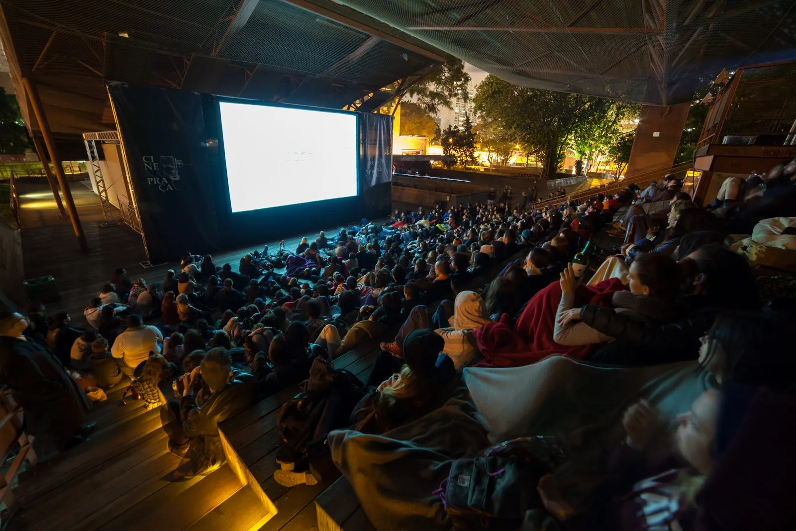 Público assistindo a um filme no telão do Cine na Praça à noite