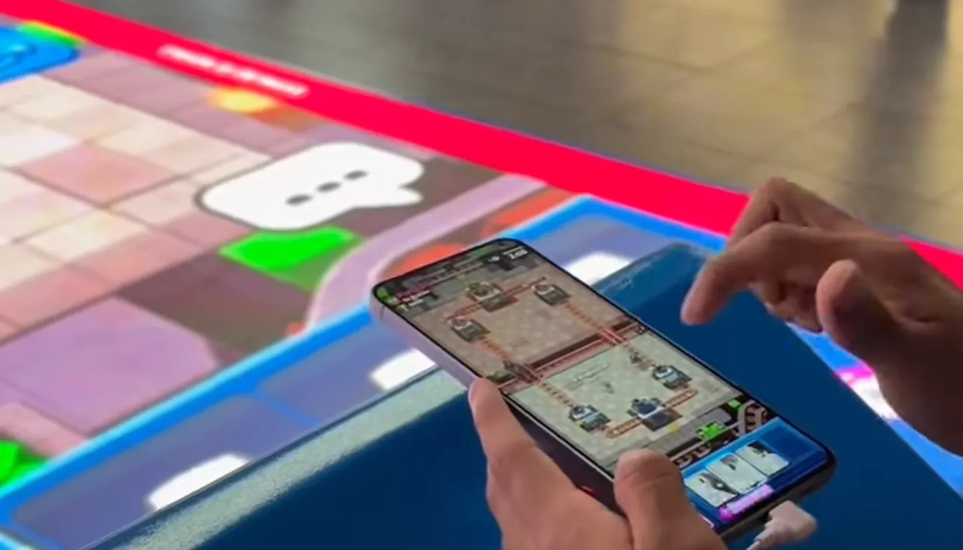 Visitante segurando o celular com uma partida de Clash Royale aberta, ao lado do piso iluminado da arena