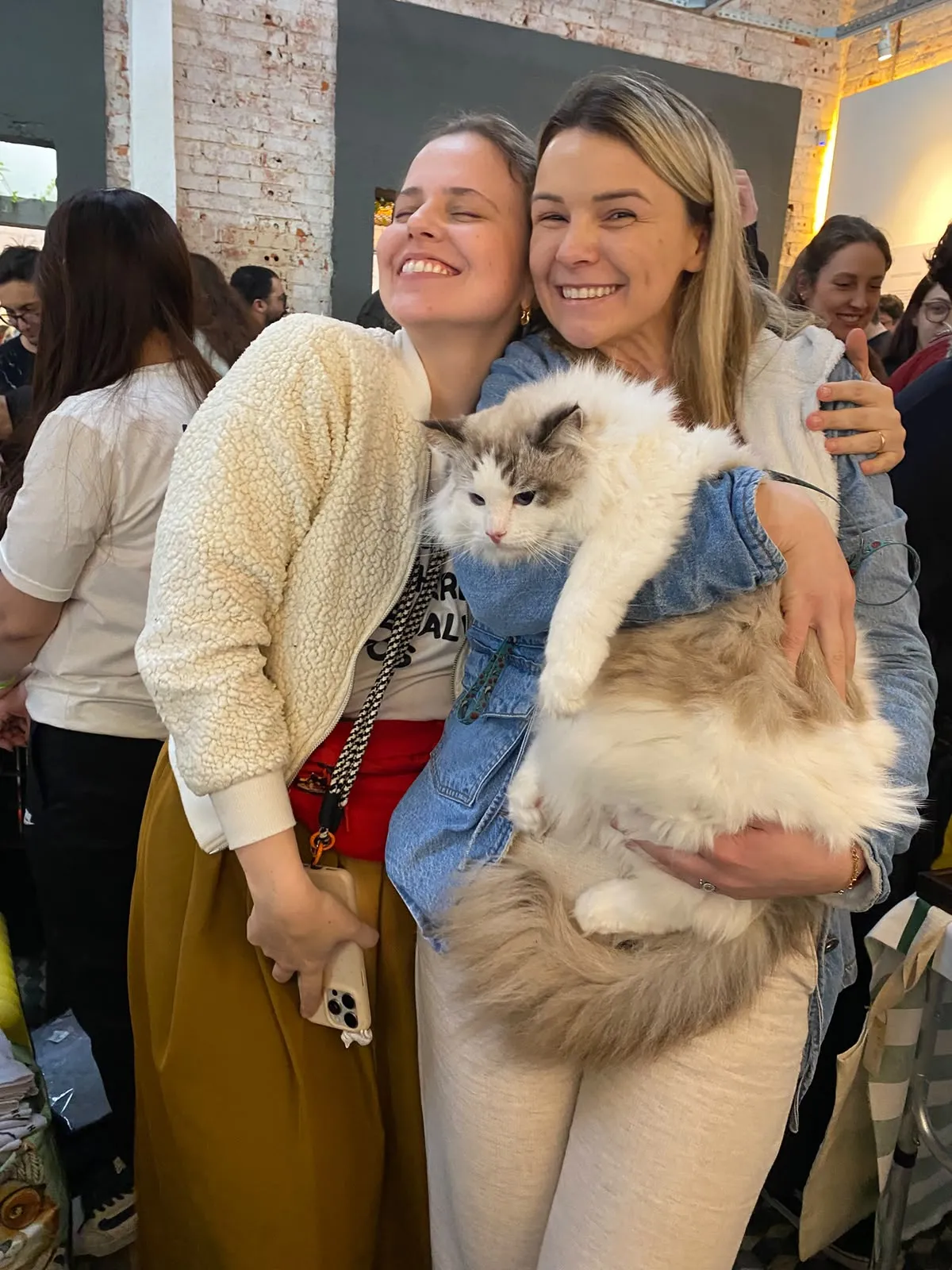 Duas visitantes sorrindo com um gato ragdoll no colo durante o encontro de gateiros da Crazy Cat Gang