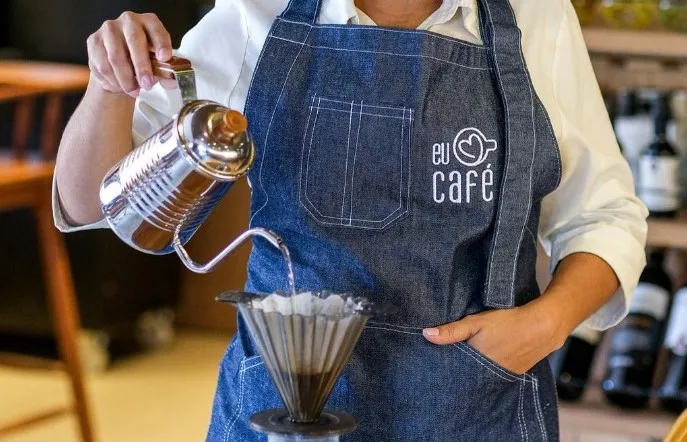 Preparo de café no filtro com chaleira e avental do Festival Eu Amo Café, em foto de divulgação de Filipe Ramos