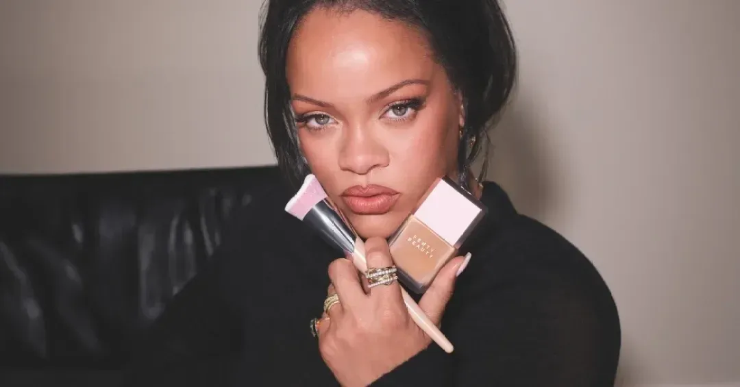 Rihanna segurando um frasco da base Fenty Beauty e um pincel chanfrado