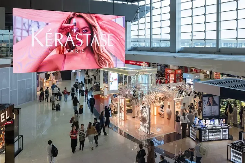 Ativação House of Gloss da Kérastase no saguão do Terminal 3 de Guarulhos, com telão da marca e passageiros circulando