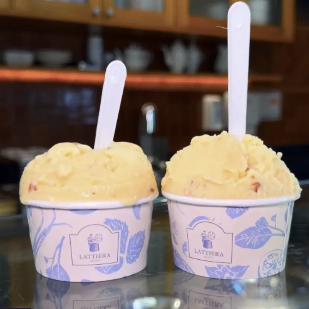 Dois copinhos de gelato amarelo da Lattiera, lado a lado com colherzinhas brancas, sobre o balcão da gelateria