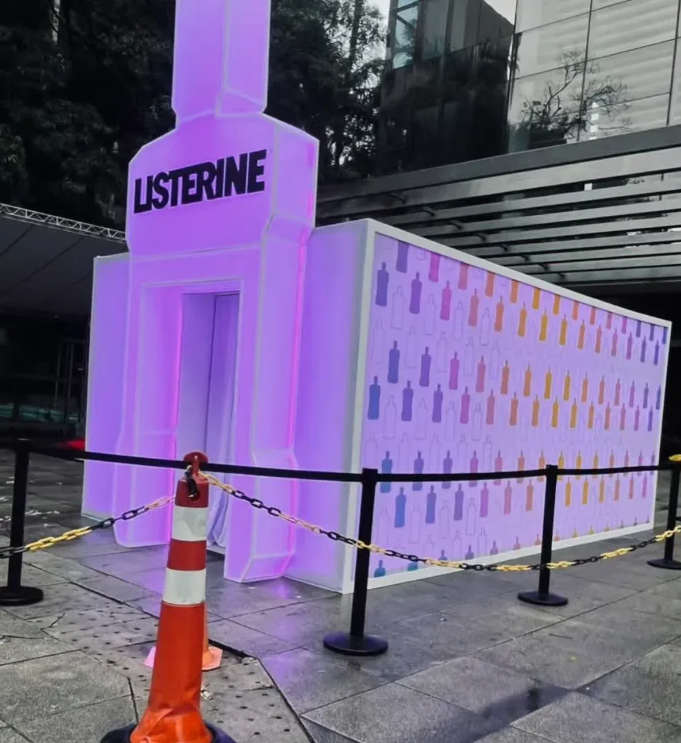 Cabine gigante em formato de frasco de Listerine, iluminada em roxo, montada na calçada da Avenida Paulista