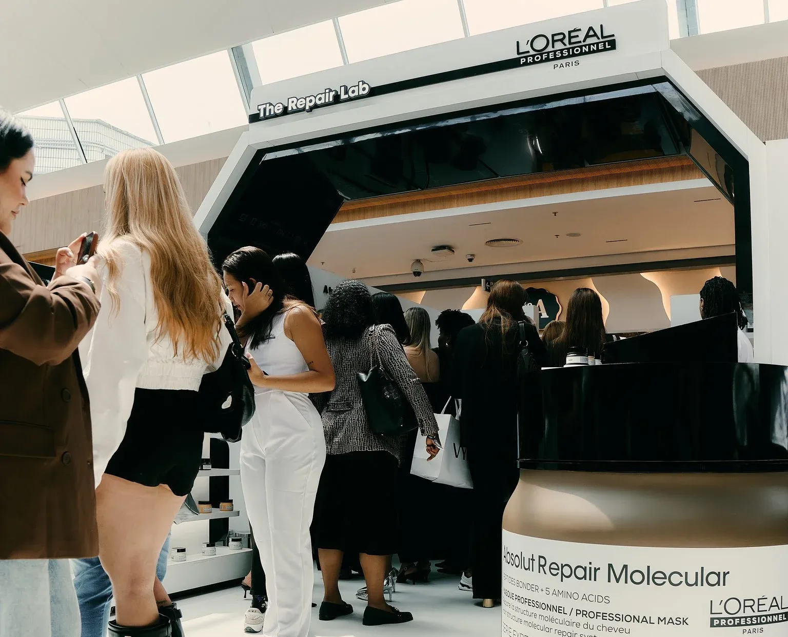 Fila de visitantes na entrada da pop-up The Repair Lab, com um pote gigante da máscara Absolut Repair Molecular em primeiro plano