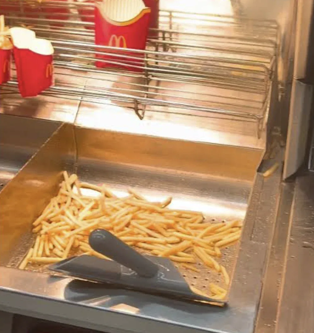 Batatas fritas no escorredor de inox, com as caixinhas vermelhas do McDonald's prontas no suporte acima