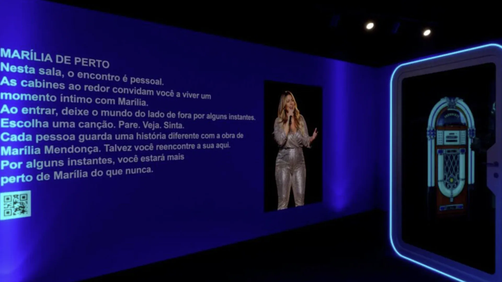 Ambiente azul da mostra no MIS com imagem de Marília Mendonça e cabine musical