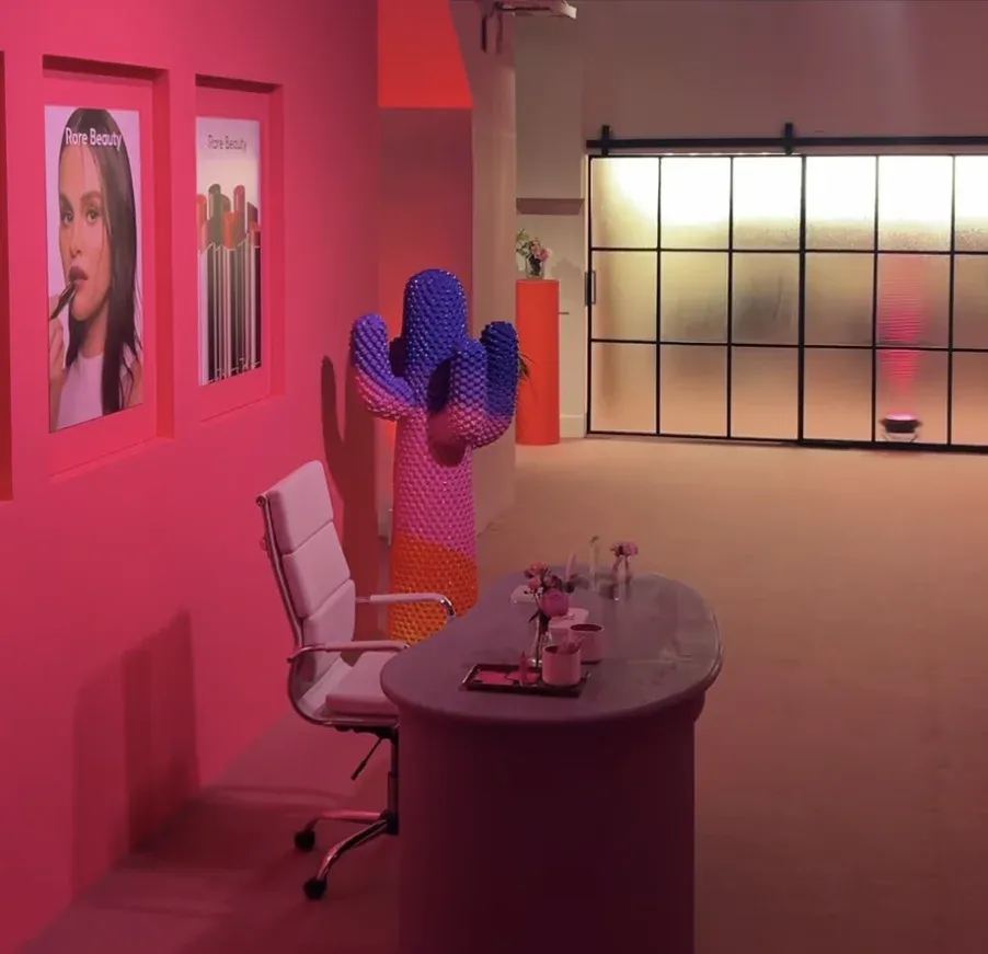 Cenário do escritório cenográfico da Rare Beauty com mesa, cadeiras e objetos em tons de rosa e bege