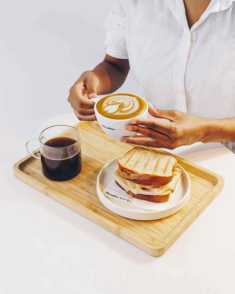 Latte com arte no leite e café coado servidos numa bandeja de madeira da The Coffee