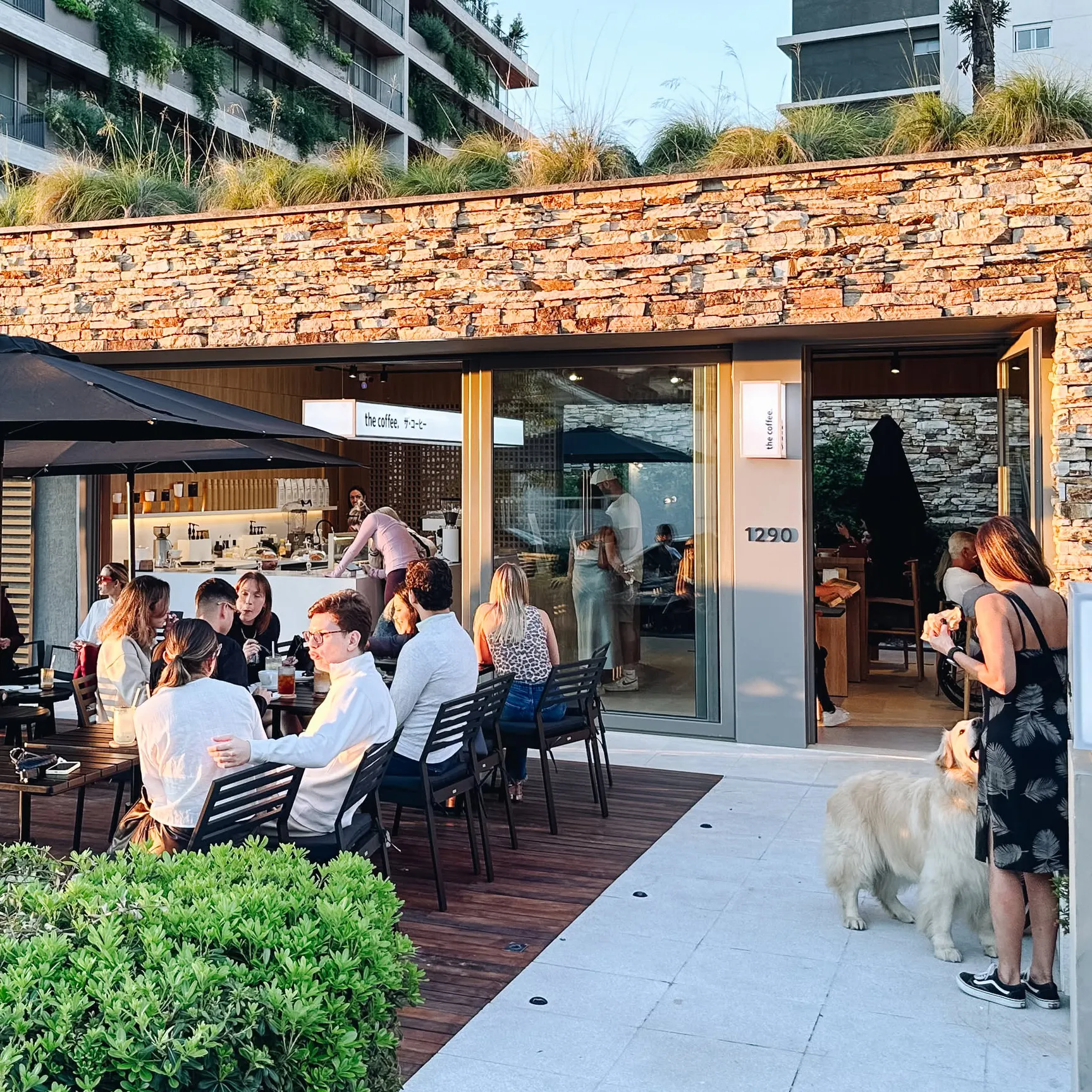 Fachada de uma loja da The Coffee com mesas na calçada e clientes tomando café no fim da tarde