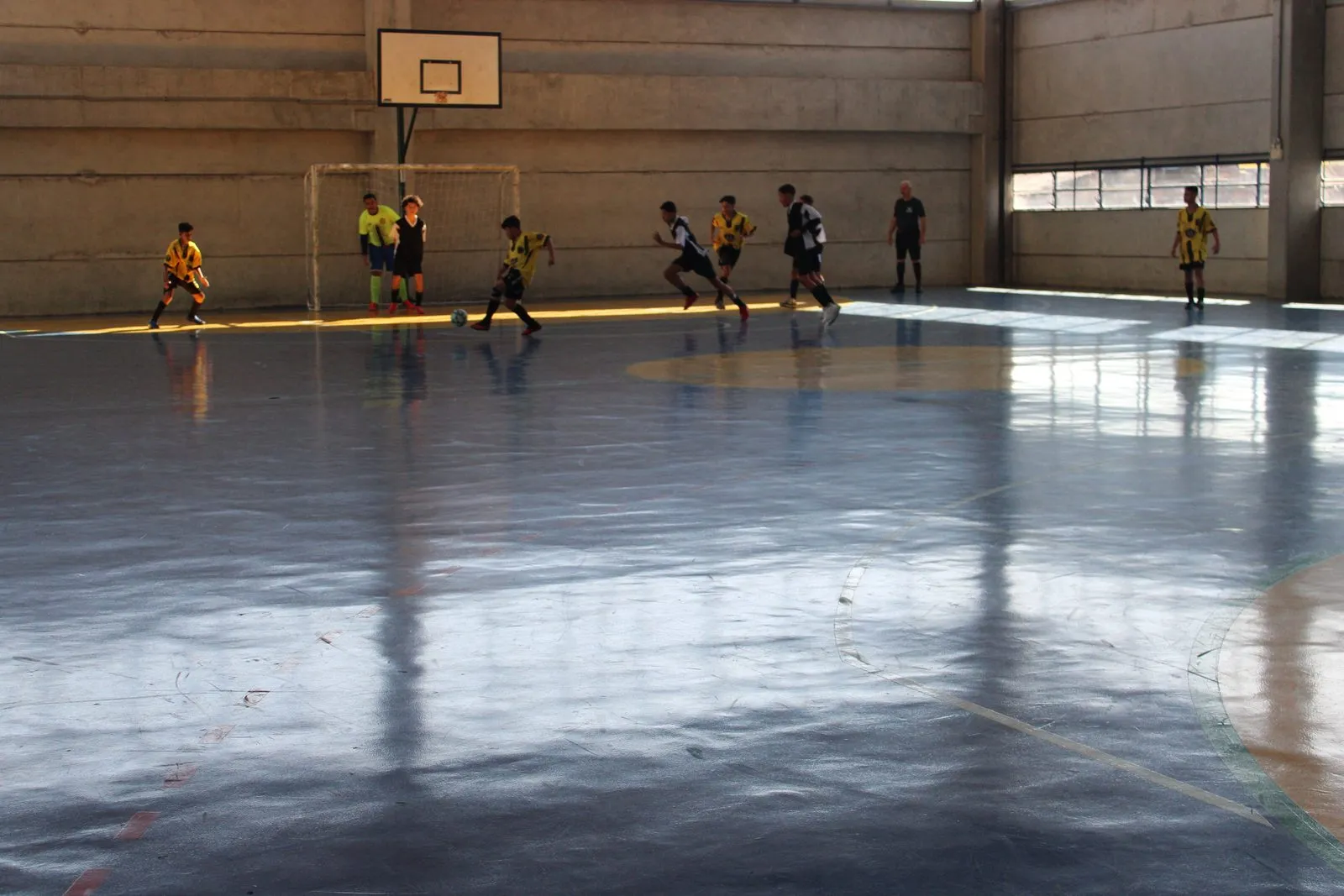 Jogadores disputando a bola em partida de futsal na quadra de um CEU